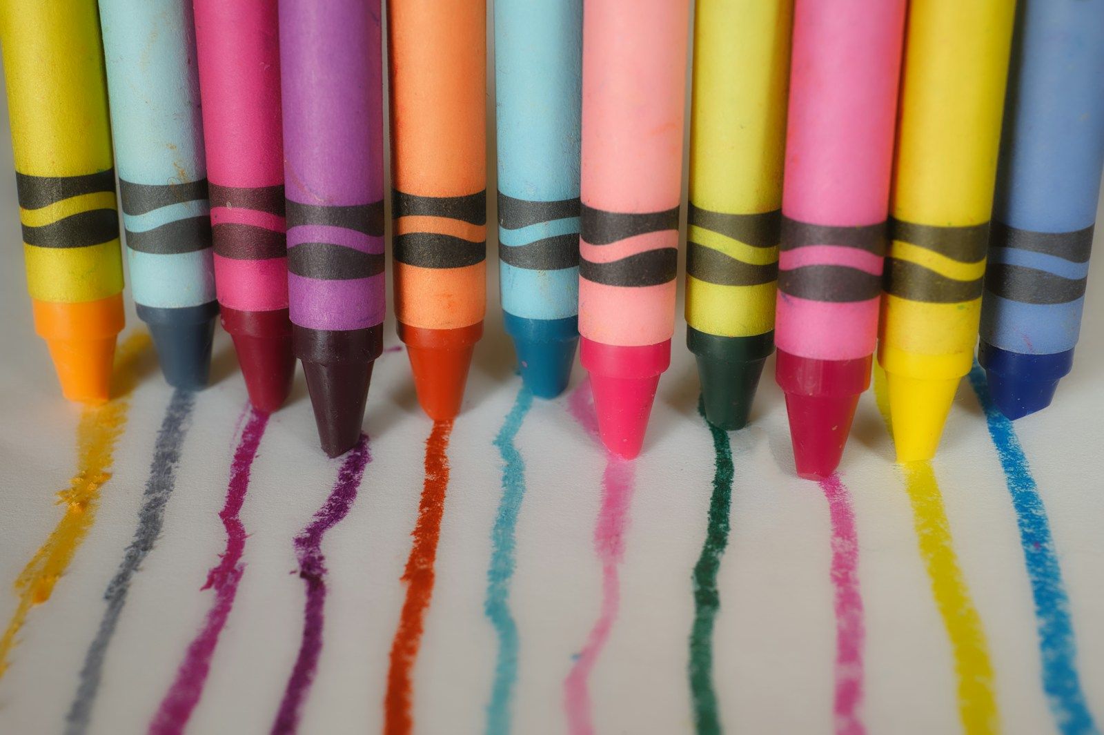Crayons standing on paper, each one having drawn a line of color down the page