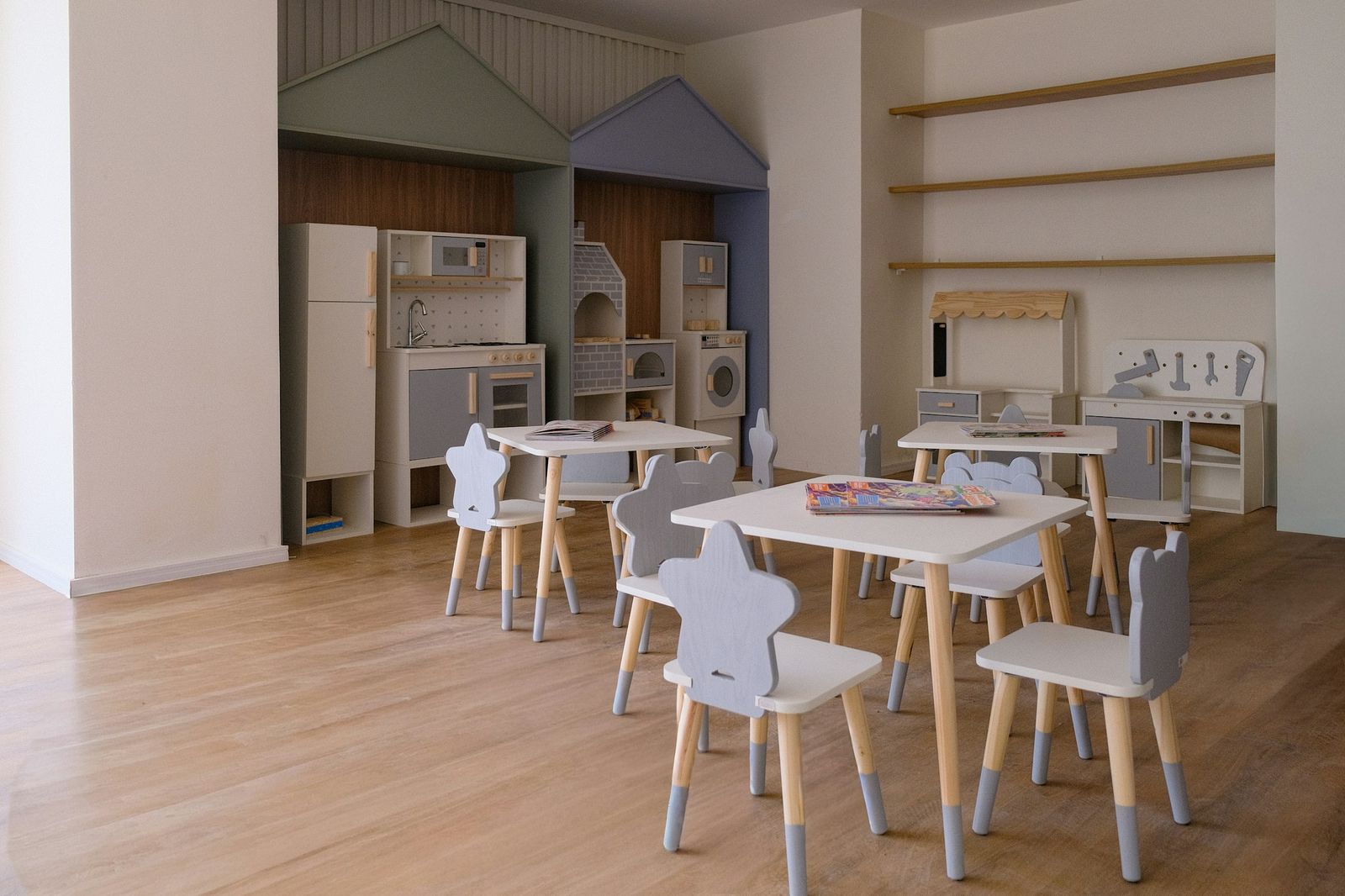 A bright play corner with small tables, chairs, and a wooden play kitchen
